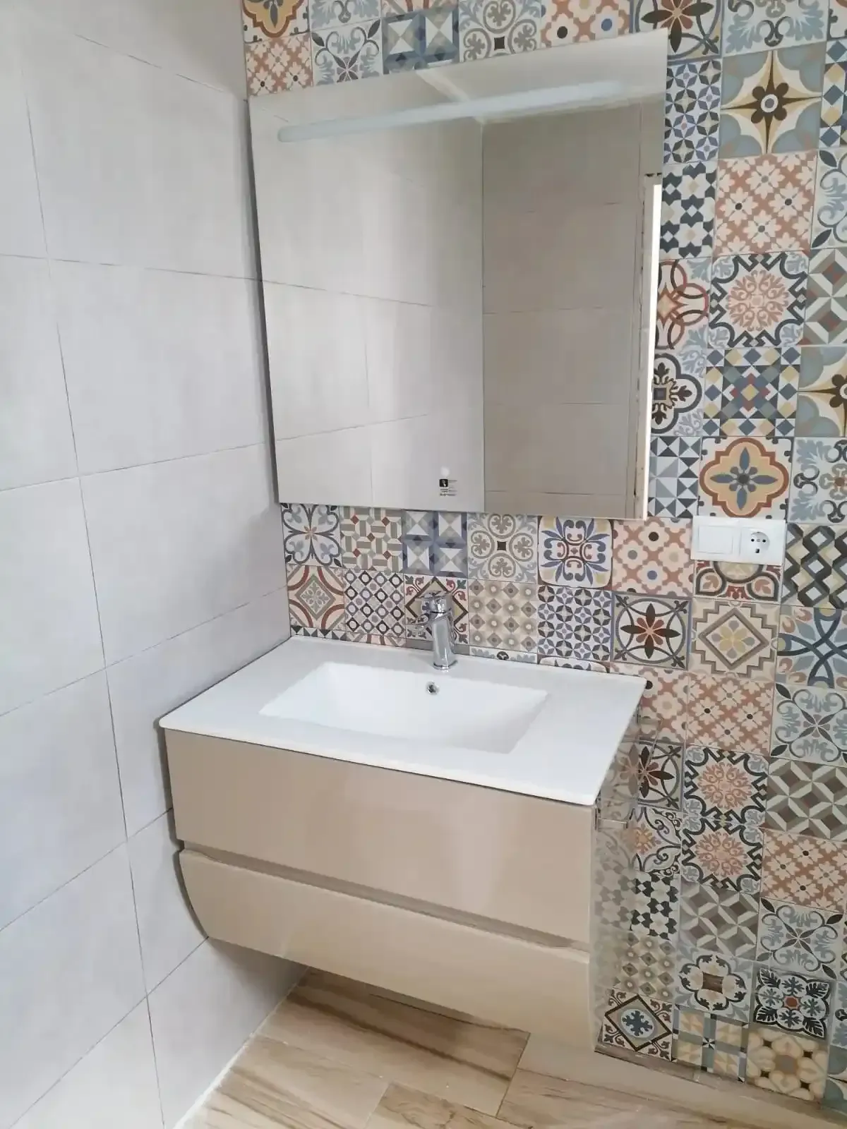 Un tocador suspendido con lavabo blanco y espejo, colocado sobre una pared revestida de azulejo.