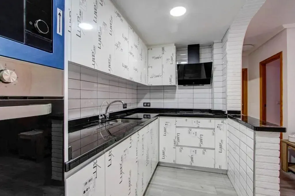 Una cocina moderna con gabinetes blancos con motivos de texto en negro, encimeras negras .