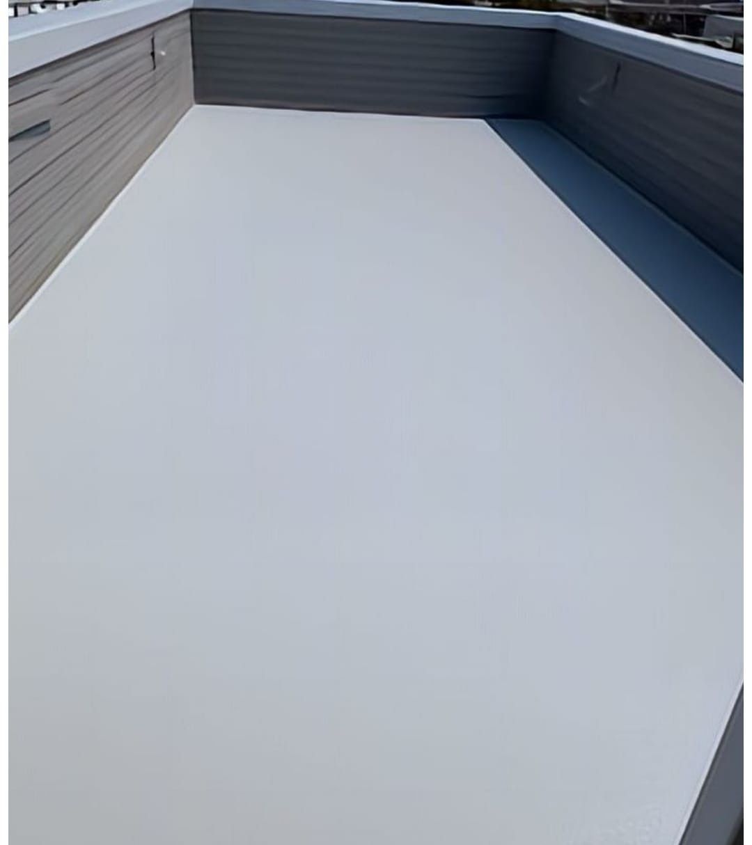 Una terraza vacía en la azotea, con suelo de color gris claro y paredes revestidas con paneles grises.