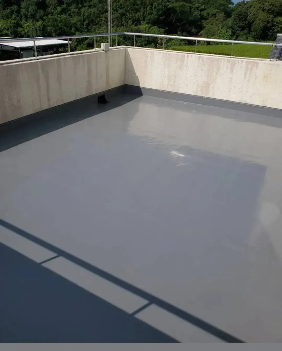 Una azotea plana con un revestimiento impermeable gris liso recién aplicado, rodeada por un muro bajo.