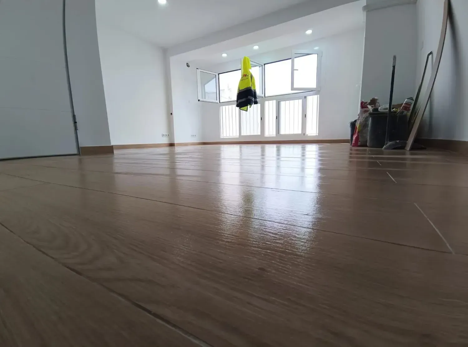 Una habitación luminosa con suelo de imitación madera pulida, paredes blancas y grandes ventanales,.