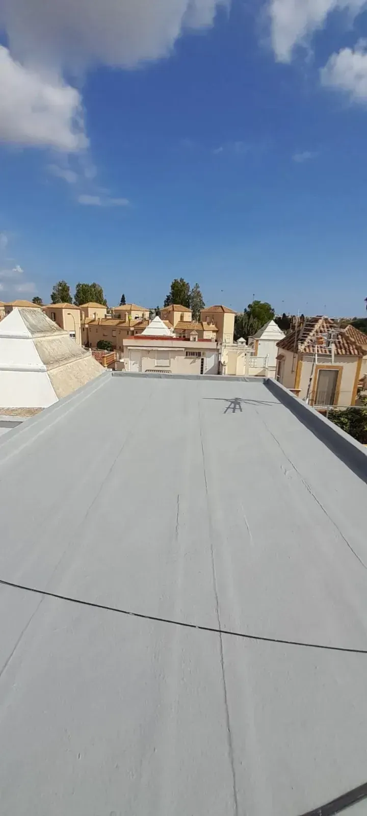 Vista desde una azotea gris y plana con vistas a un cementerio histórico con tumbas de piedra blanca bajo un cielo azul.