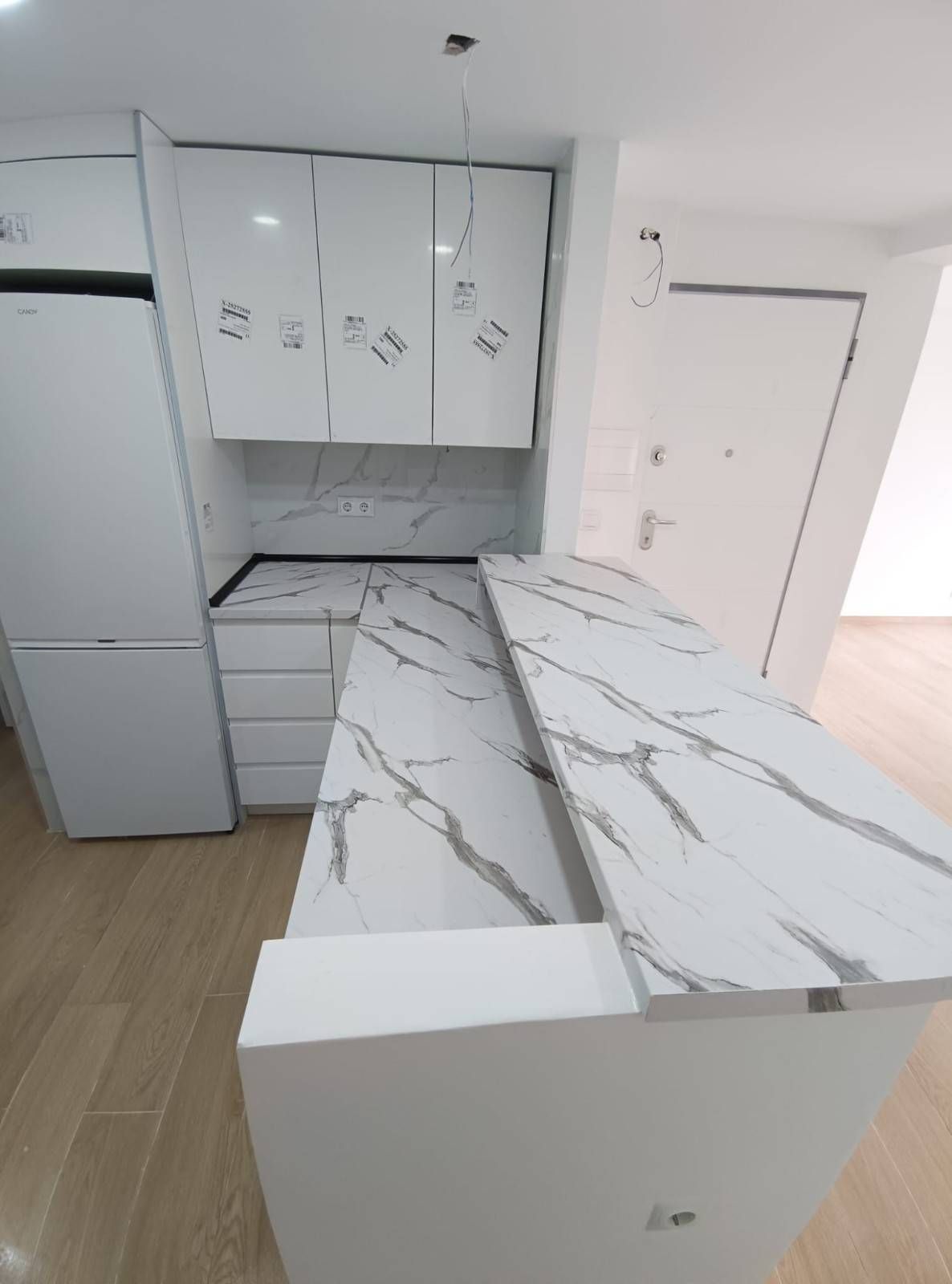 Una cocina moderna con armarios blancos, un frigorífico y una encimera de dos niveles con diseño de mármol blanco.