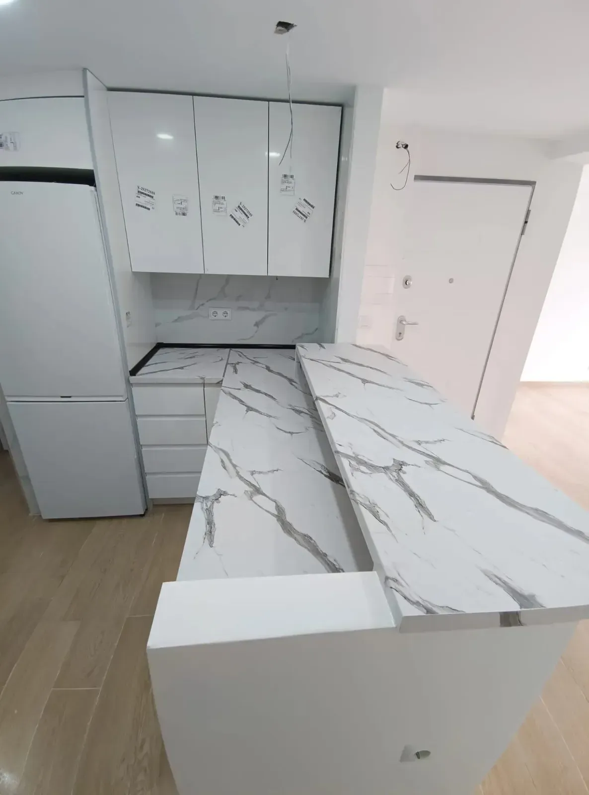 Una cocina moderna con gabinetes blancos, un refrigerador blanco y una isla con encimera con diseño de mármol.