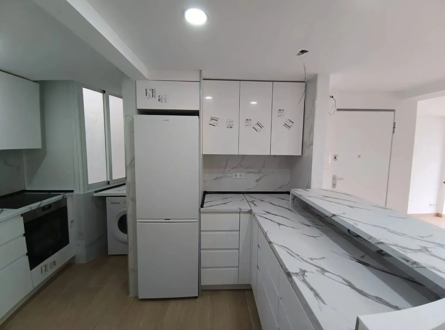 Cocina moderna de color blanco con encimeras con diseño de mármol, electrodomésticos integrados y suelo de madera clara.