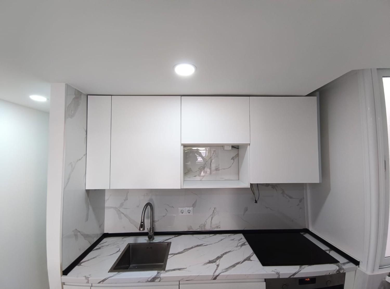 Una pequeña cocina moderna con armarios blancos, encimera y protector contra salpicaduras.