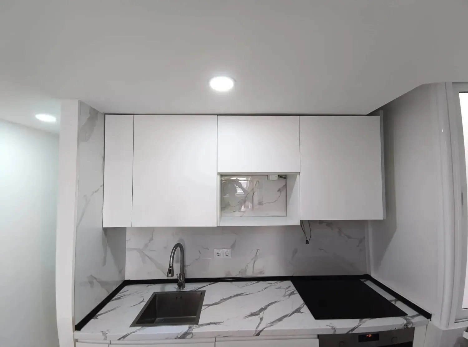 Una cocina moderna con gabinetes blancos, encimera y protector contra salpicaduras con diseño de mármol, fregadero.