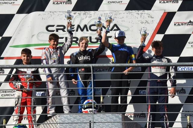 Die Sieger auf dem Podium des Cremona Circuit. Fünf Kartfahrer heben ihre Trophäen in die Höhe. Im Hintergrund die italienische Flagge.
