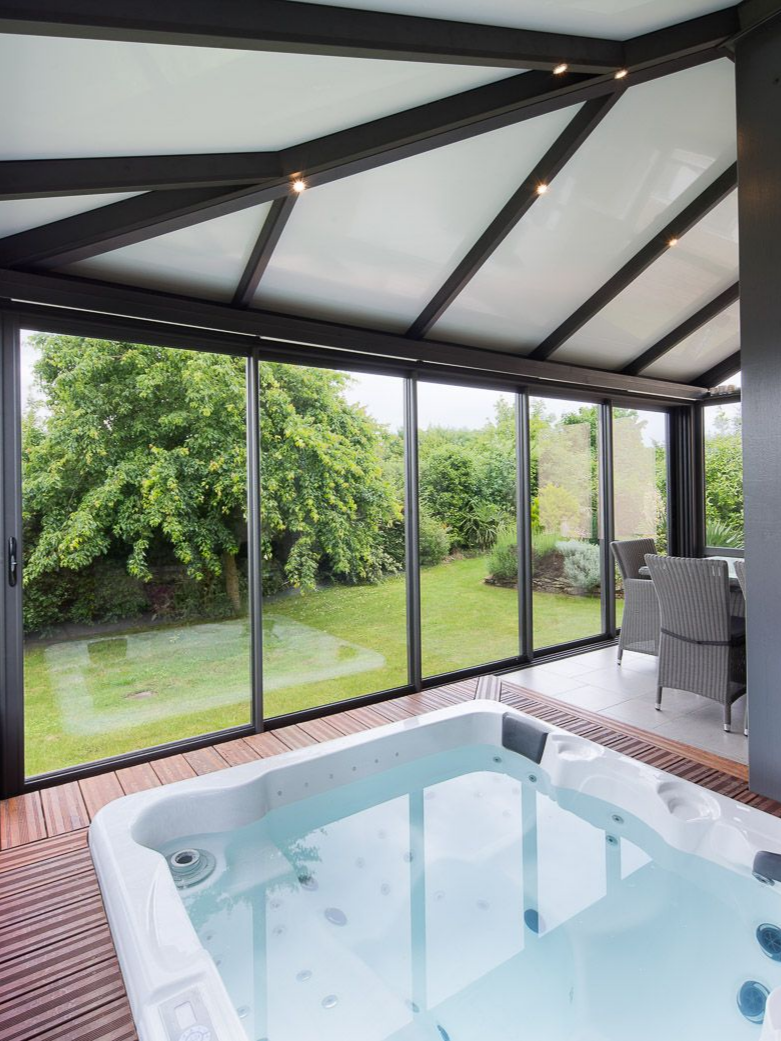 Véranda abritant un salon de jardin et un spa