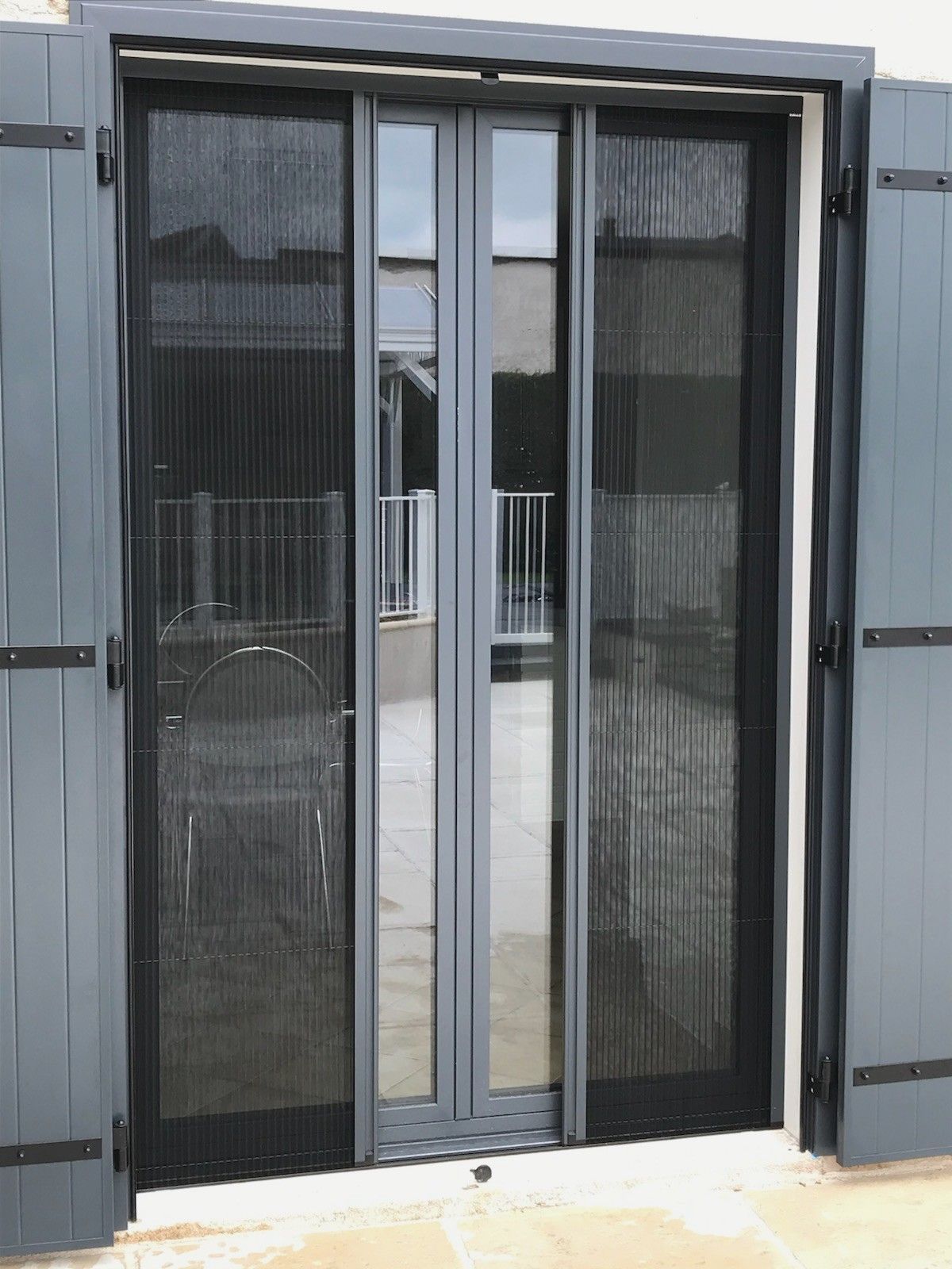 Porte-fenêtre avec moustiquaire noire, cadre gris et volets