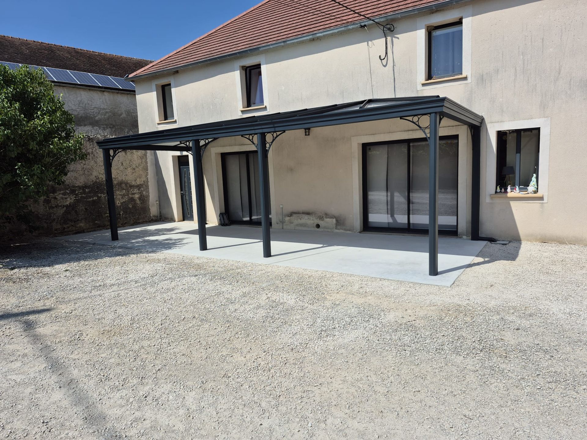 Une pergola grise ombrage une terrasse en béton