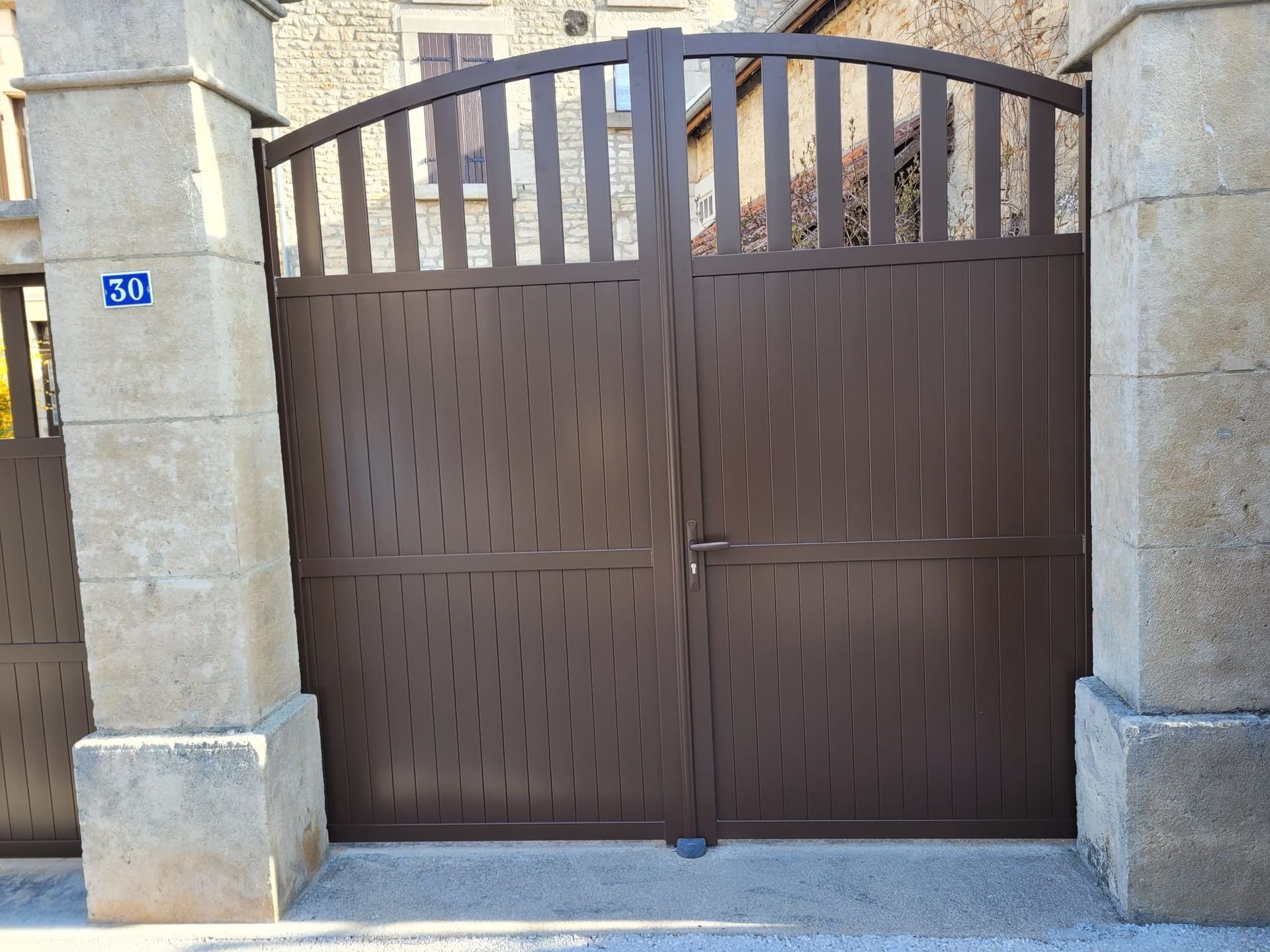 Double portail en métal marron entre des piliers en pierre