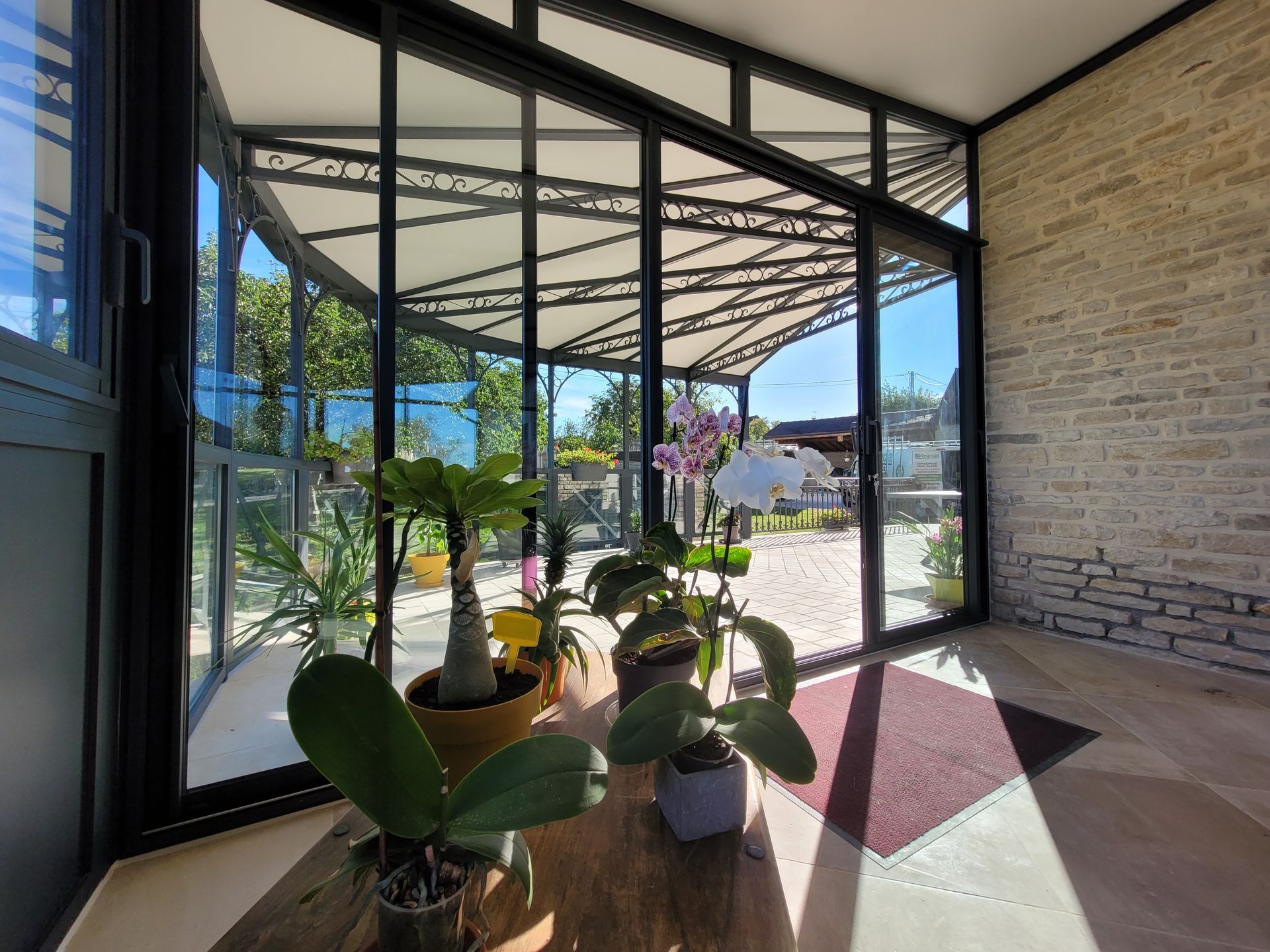 Véranda avec baies vitrées incurvées, plantes et mur de briques
