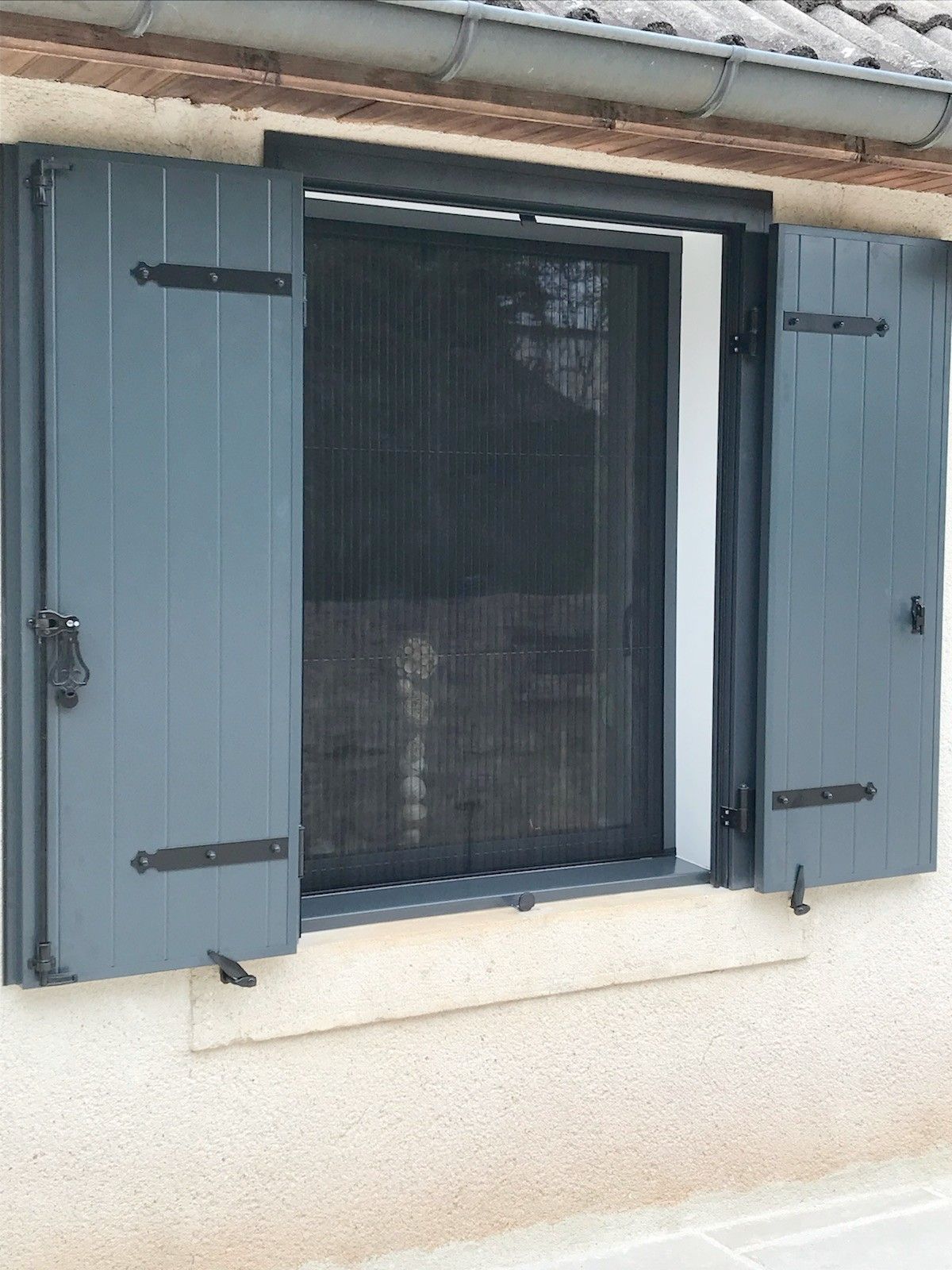 Des volets bleus s'ouvrent à côté d'une fenêtre munie d'un écran noir