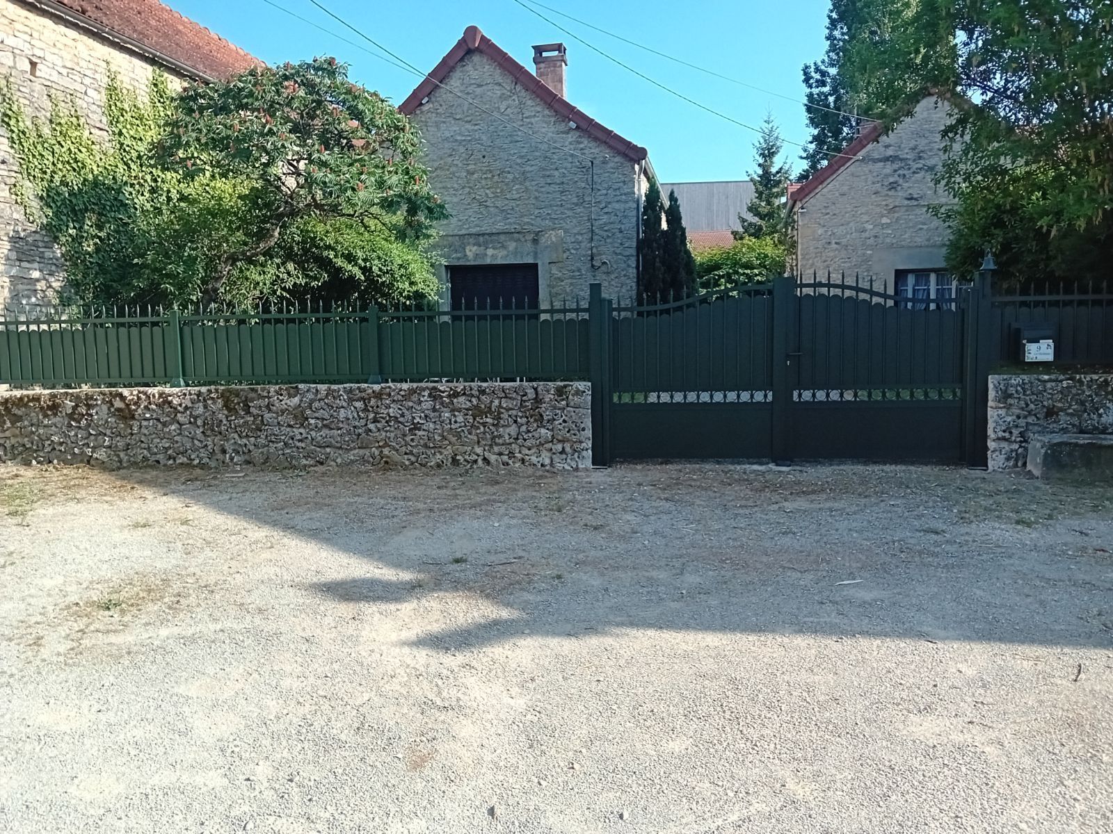 Maison en pierre avec clôture et portail verts, allée de gravier