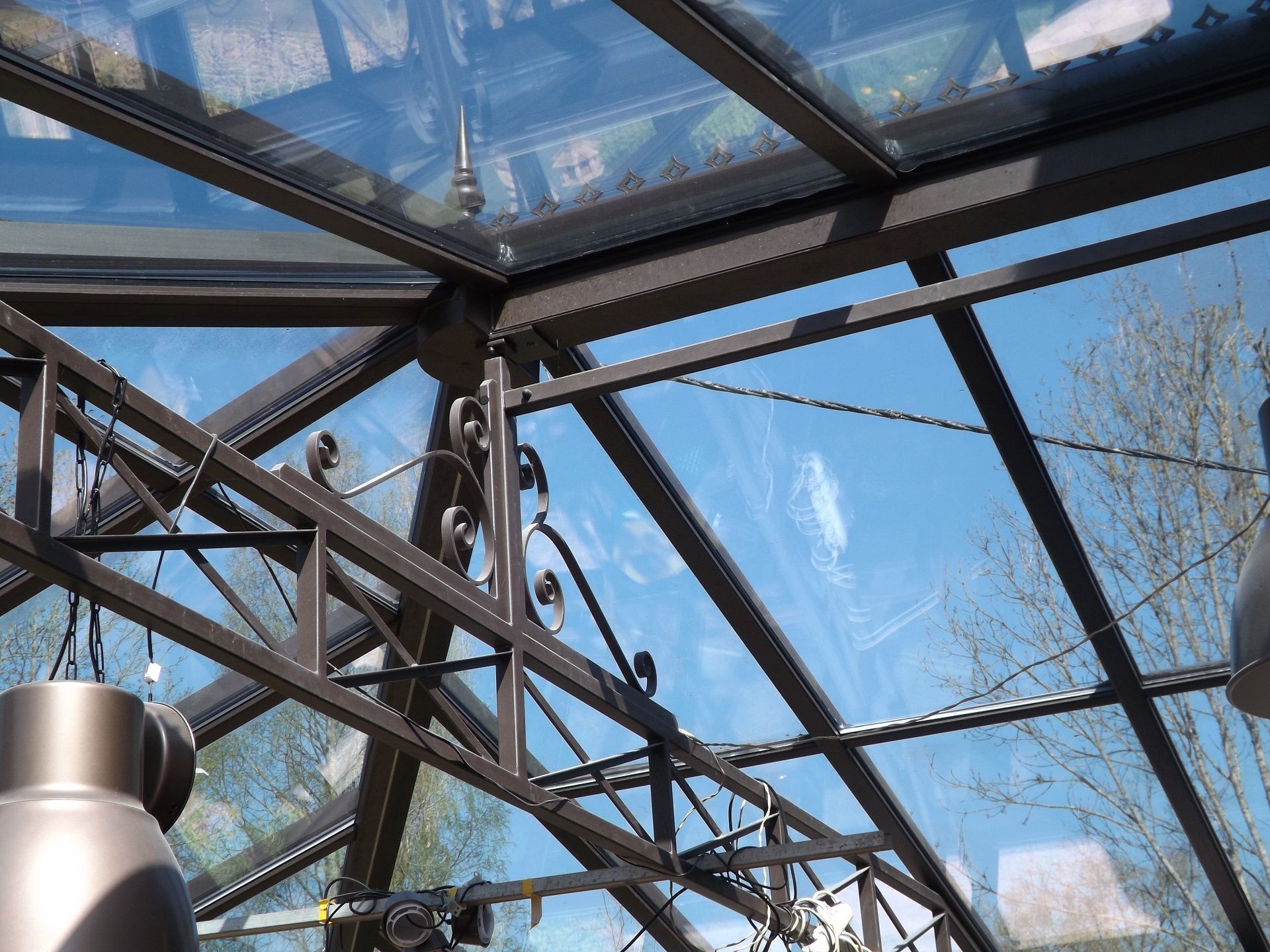 Vue intérieure d'une serre à structure métallique sombre et panneaux de verre. Le ciel bleu est visible à travers le toit