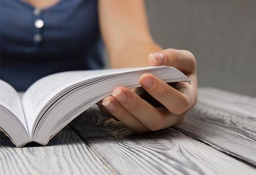 Una mujer está leyendo un libro en una mesa de madera.