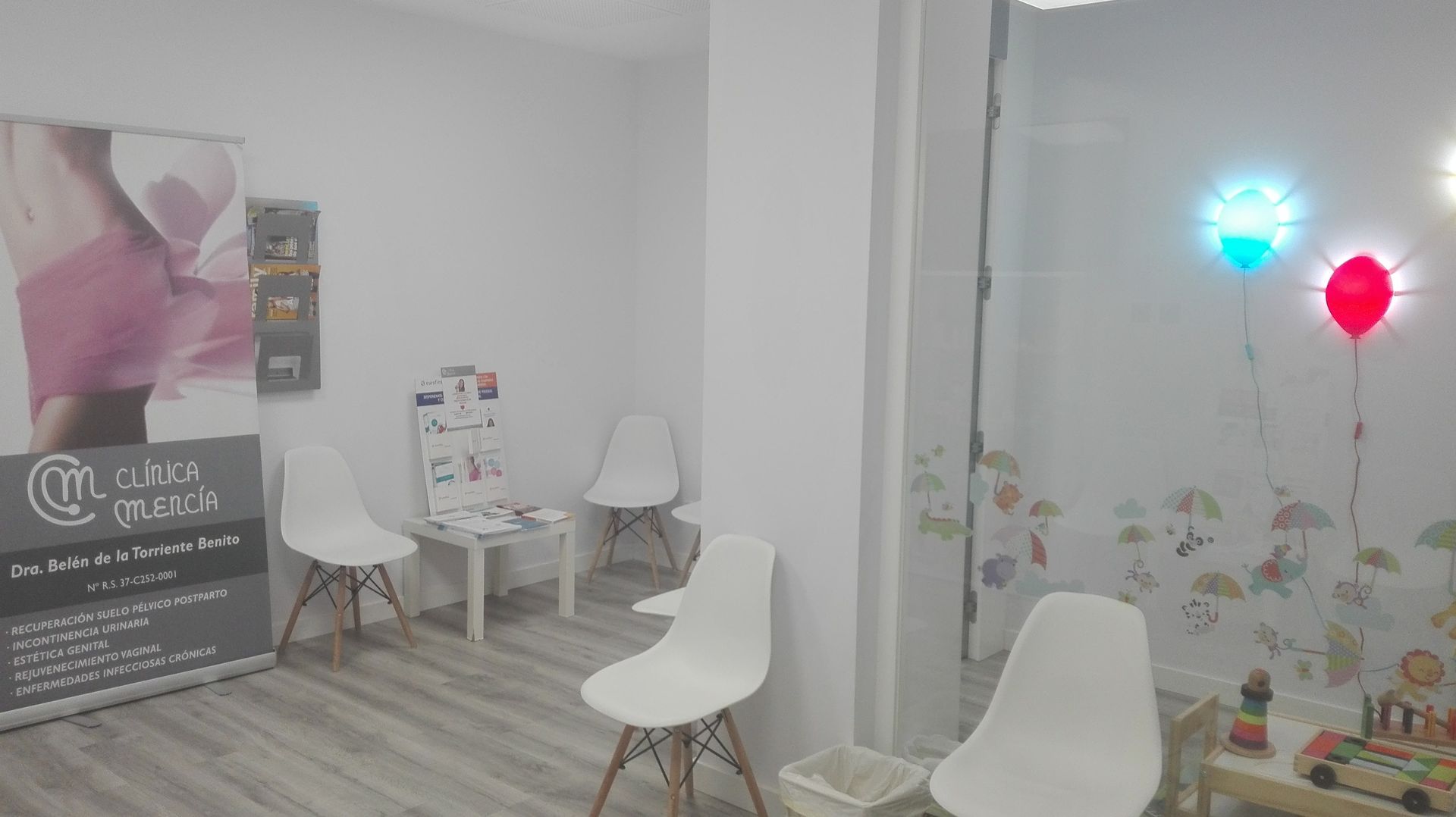 Una sala de espera con sillas blancas, una mesa y un cartel en la pared.