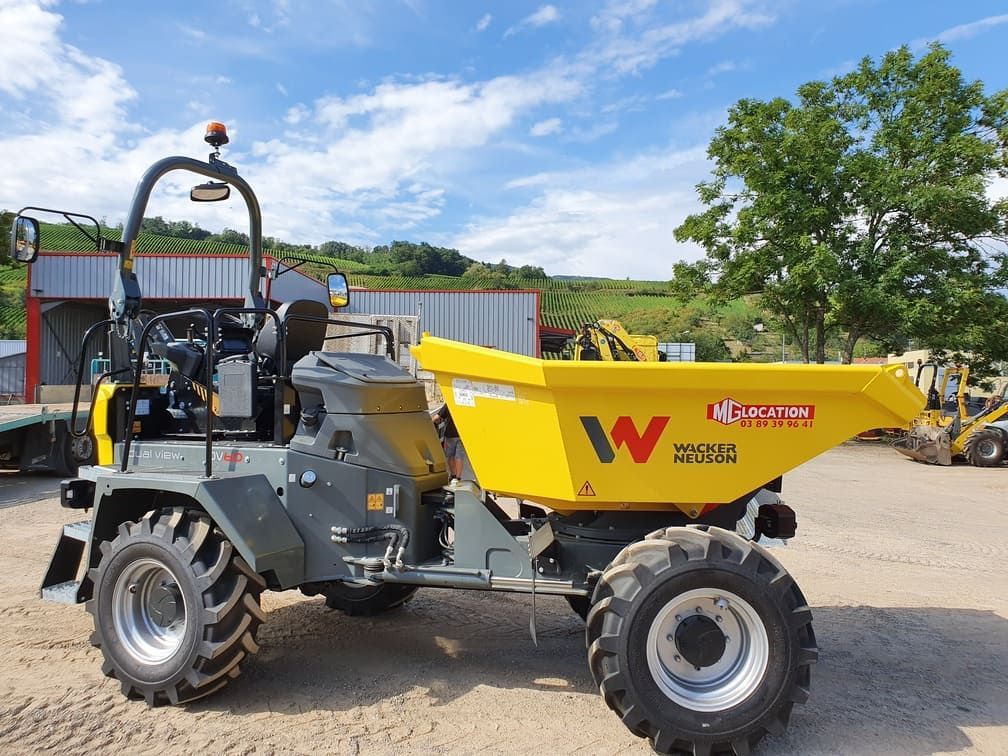 Camion-benne Wacker Neuson jaune stationné à l'extérieur sur un terrain vague sous un ciel bleu