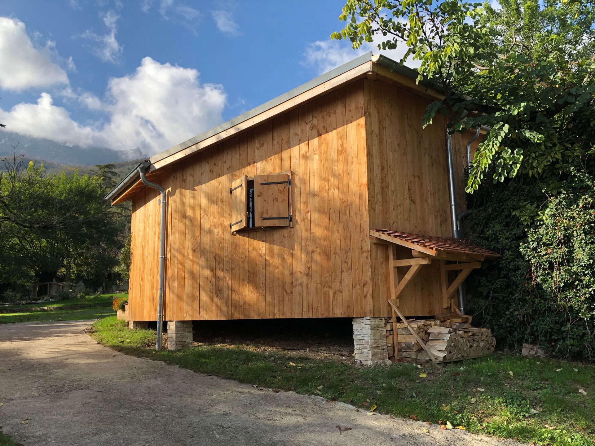 Petite construction en bois avec des volets et un abri pour les bûches, avec un toit en pente.
