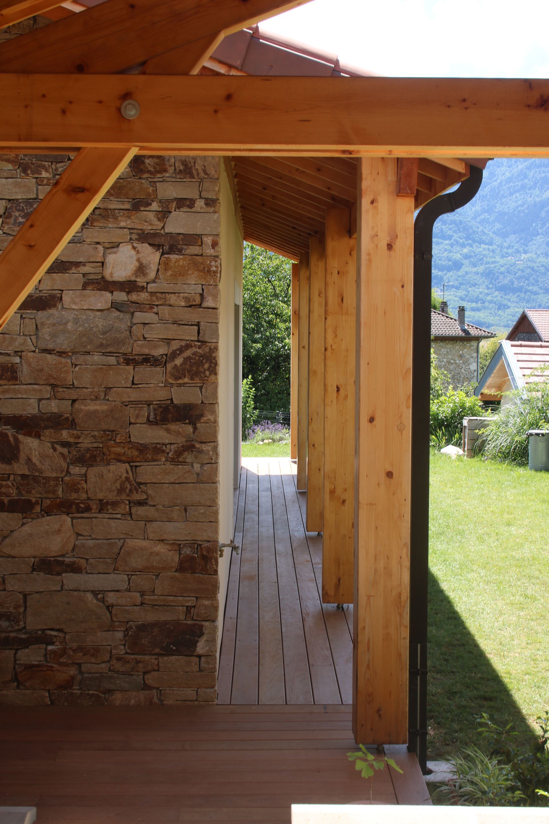 Poutres apparentes pour soutenir l'avancée d'un toit au-dessus d'un chemin de terrasse en bois.