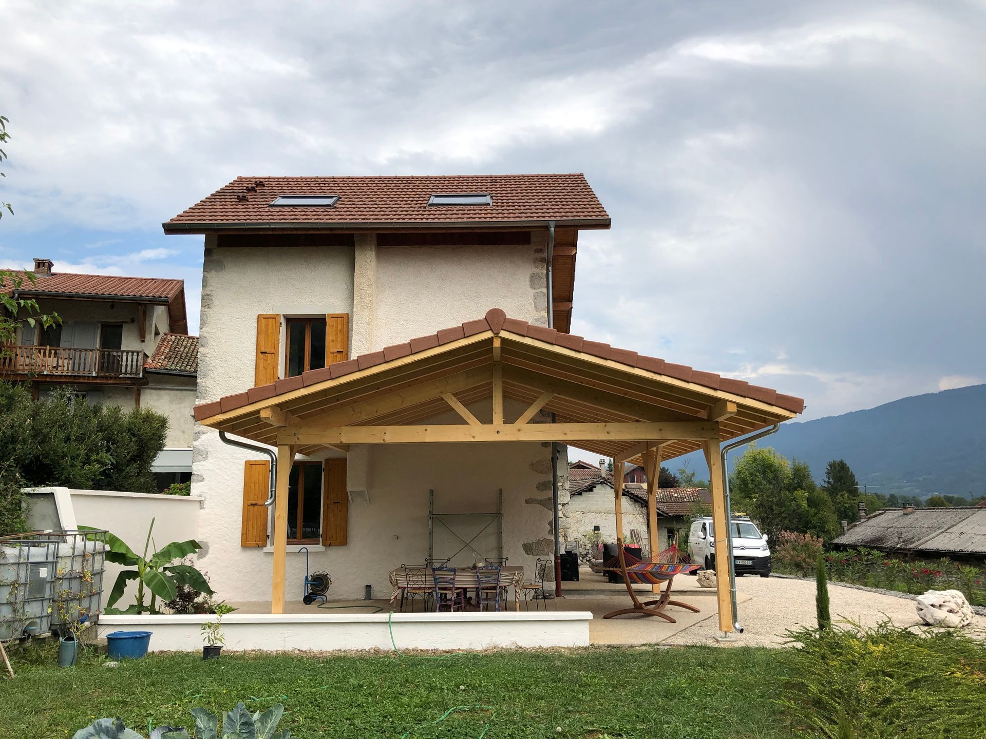 Préau construit au-dessus d'une terrasse et le long de la façade.