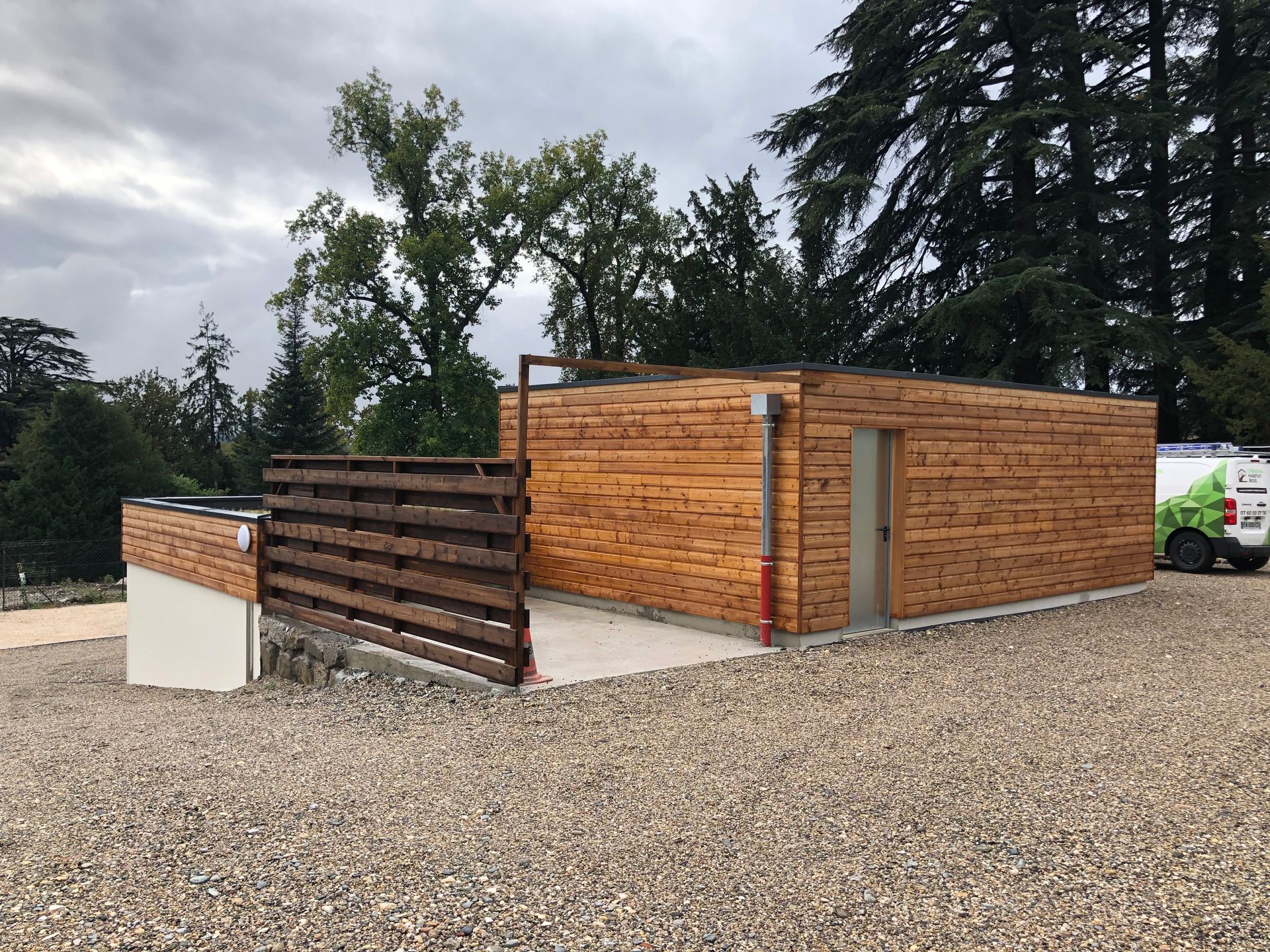Bardage en bois autour d'un bâtiment avec une clôture en bois le long d'un accès.