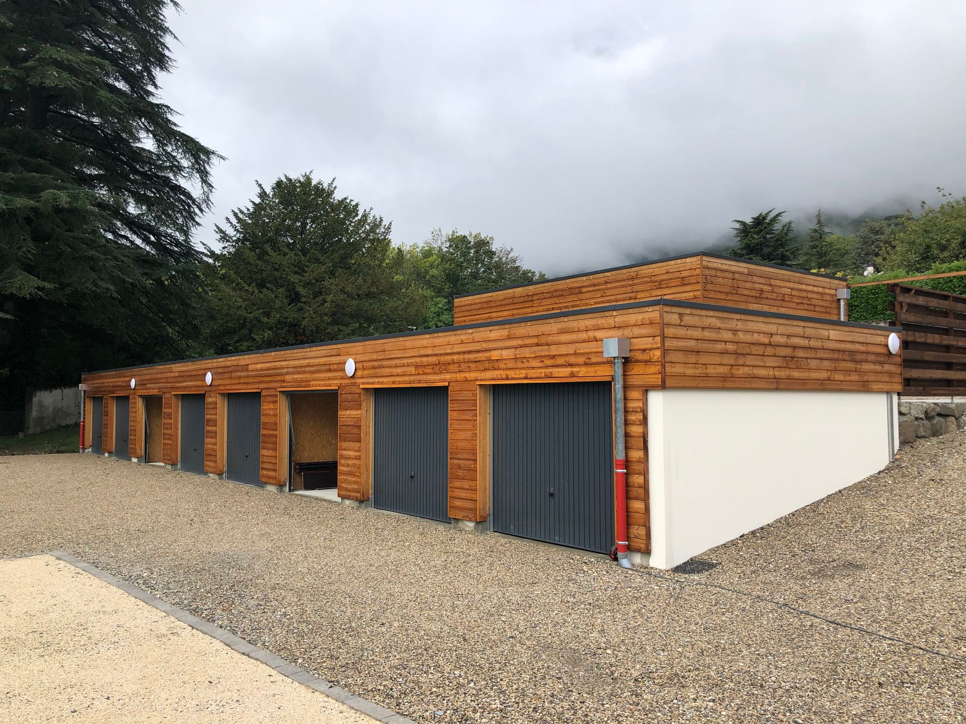 Plusieurs garages avec du bardage en bois et un bâtiment en hauteur en arrière-plan.