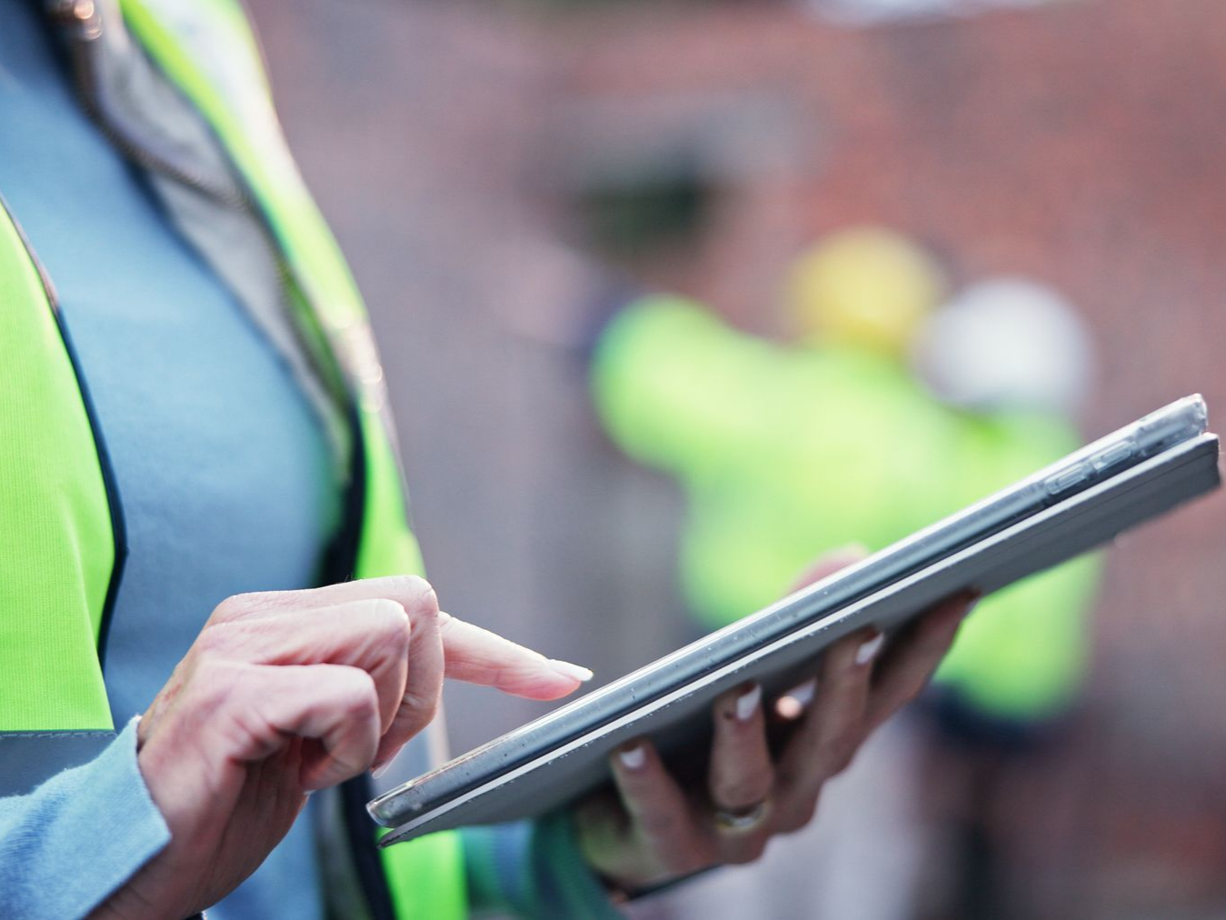 Une personne portant un gilet jaune utilise une tablette en extérieur.