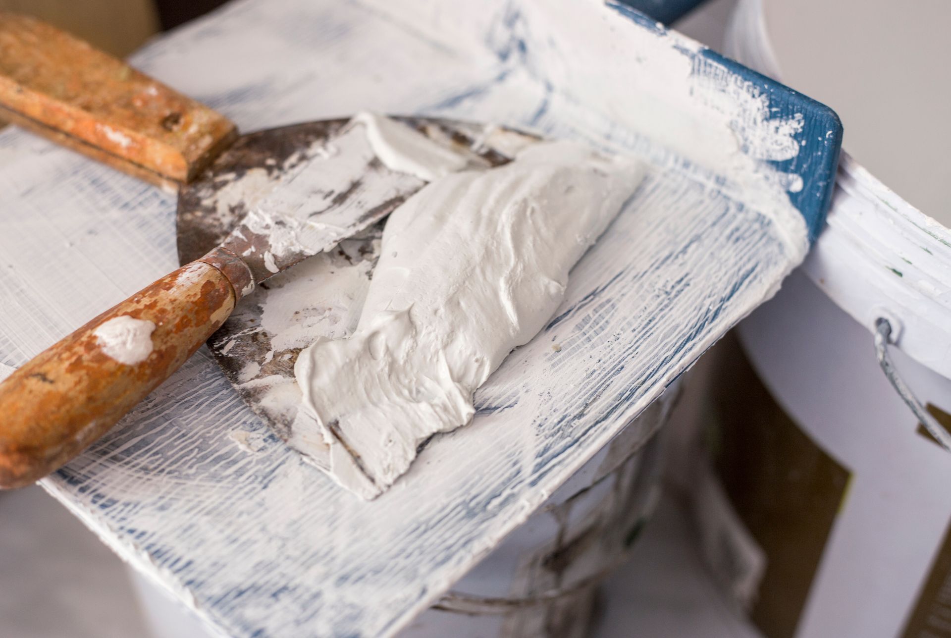 Un couteau à mastic en métal à manche en bois repose sur un seau de peinture.