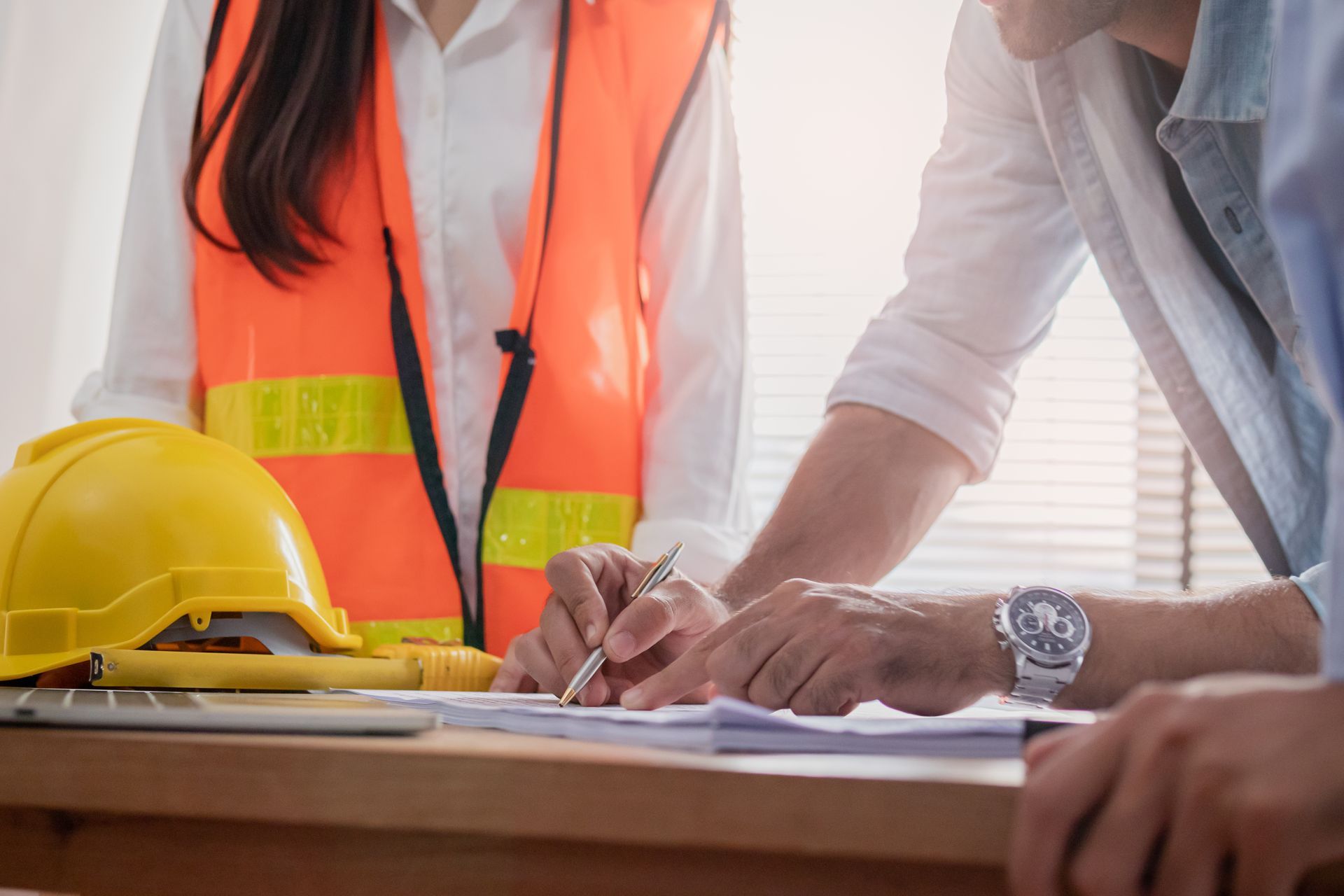 Une personne portant un gilet haute visibilité et une autre personne écrit sur un document à un bureau.
