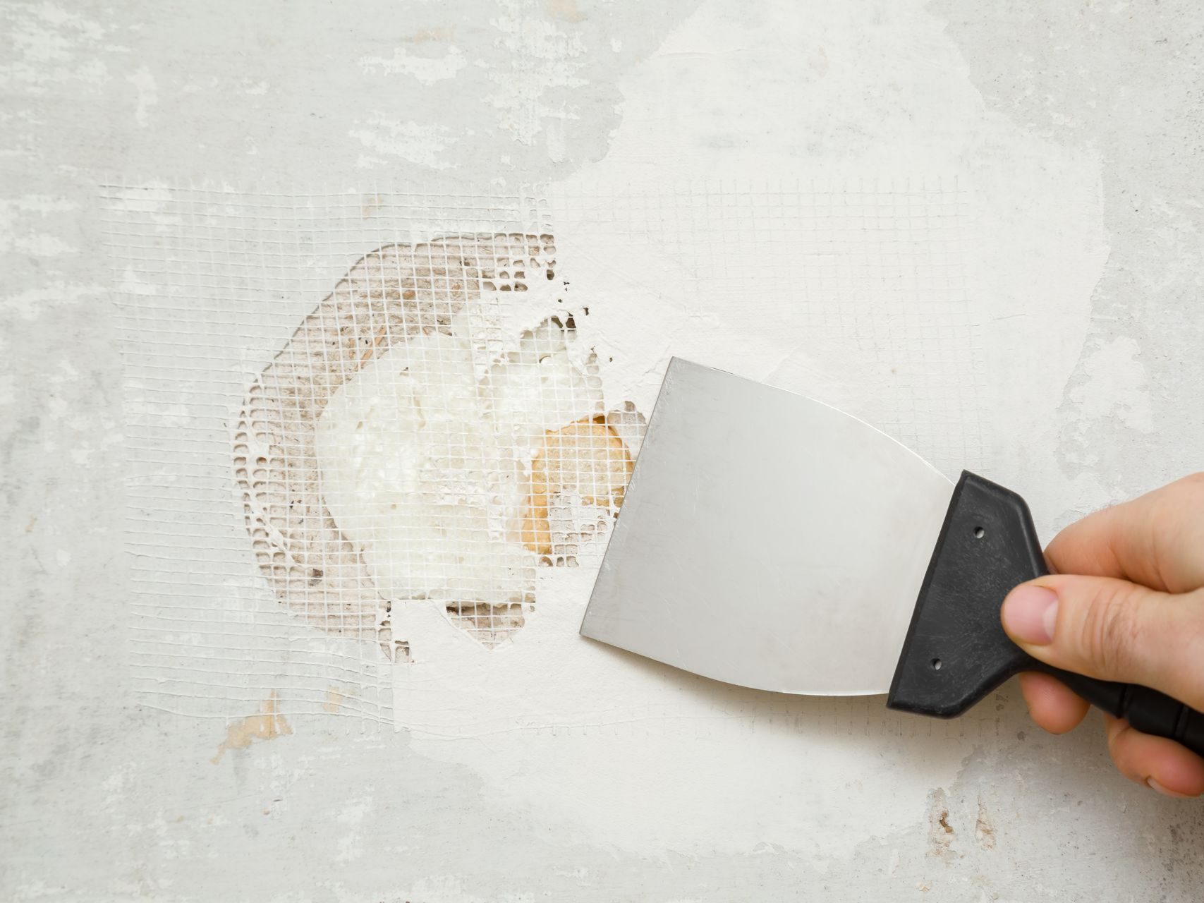 Une personne utilise un couteau à mastic en métal pour gratter le vieux plâtre.