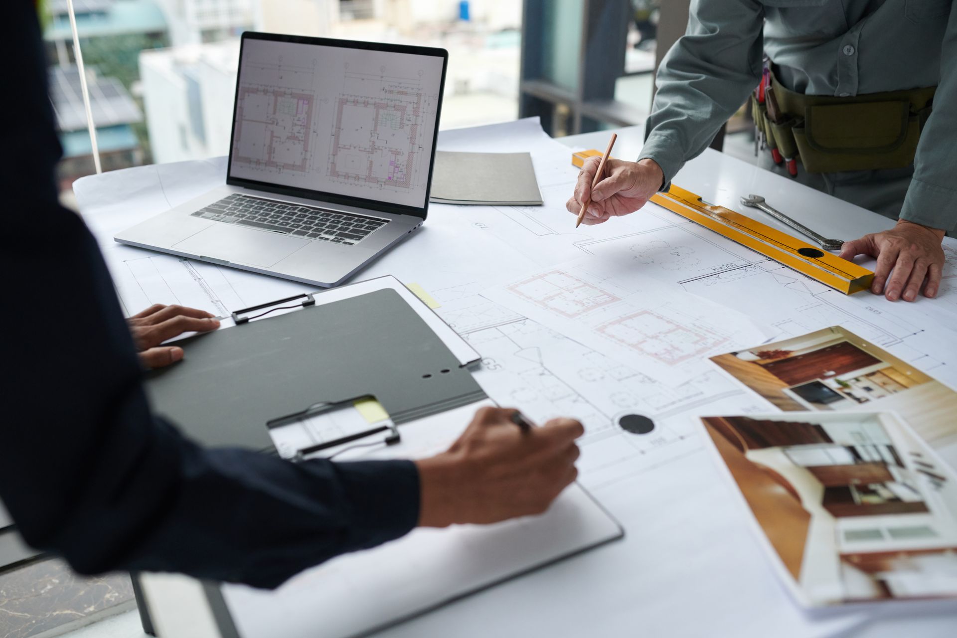 Deux personnes collaborent sur des plans architecturaux à un bureau, à l'aide d'un ordinateur portable et d'un bloc-notes.