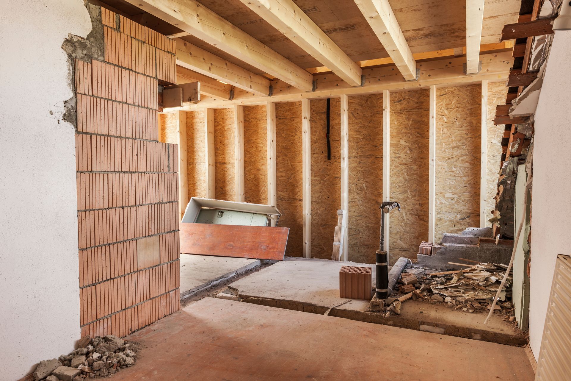 Intérieur d'une pièce en construction, montrant des briques apparentes, des poutres en bois et des murs nus.