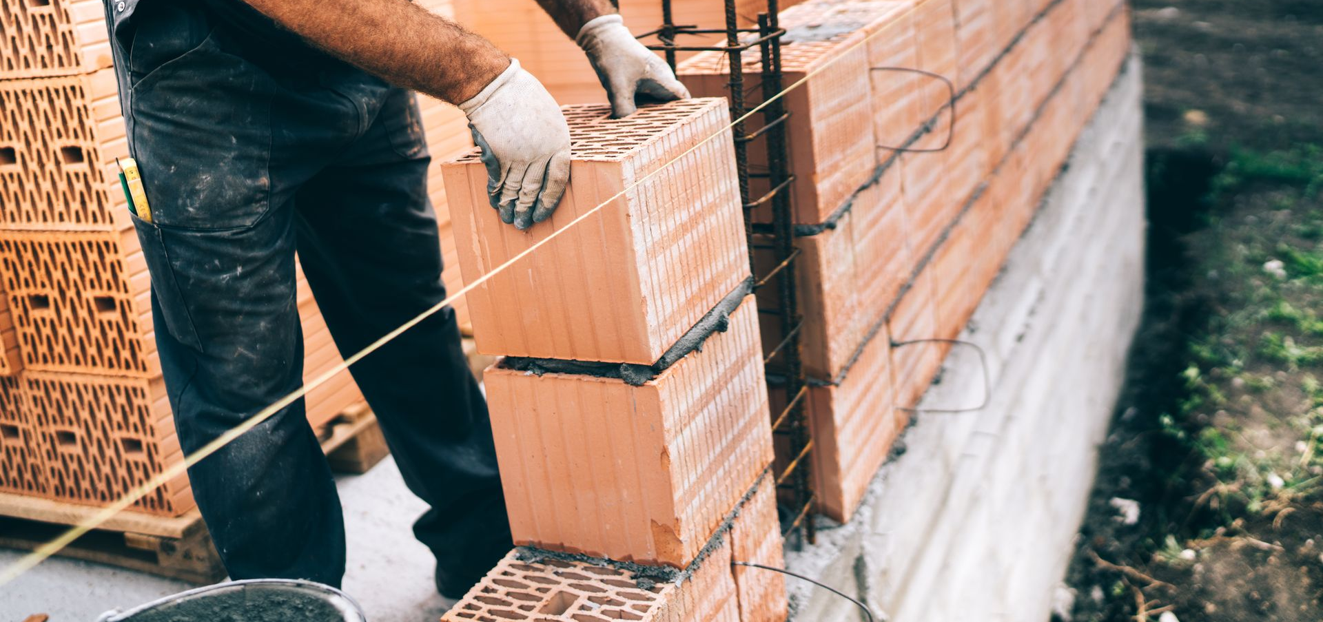 Un ouvrier du bâtiment portant des gants pose des briques sur un mur.