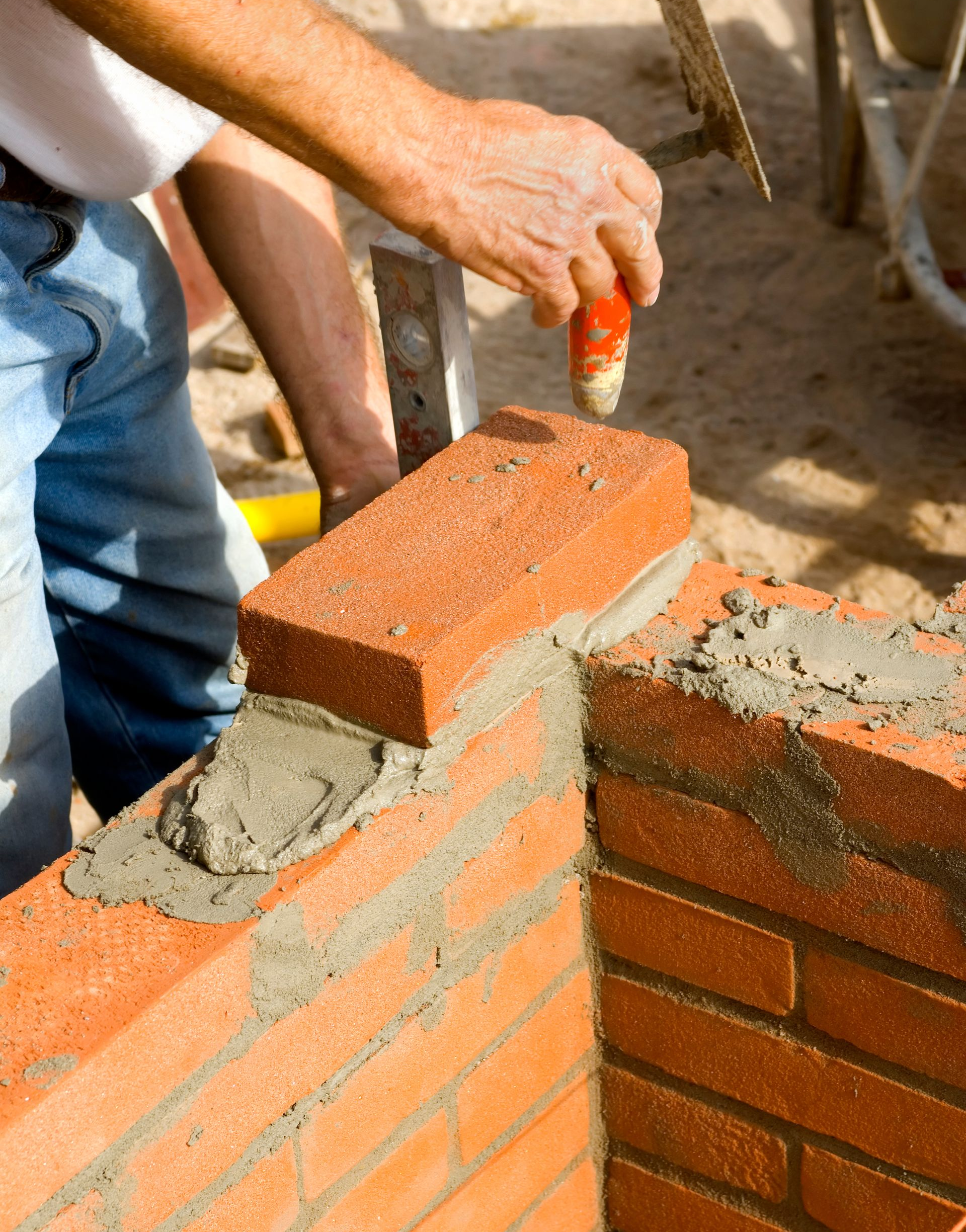 Une personne posant une brique, appliquant du mortier, construisant un mur d'angle en briques.