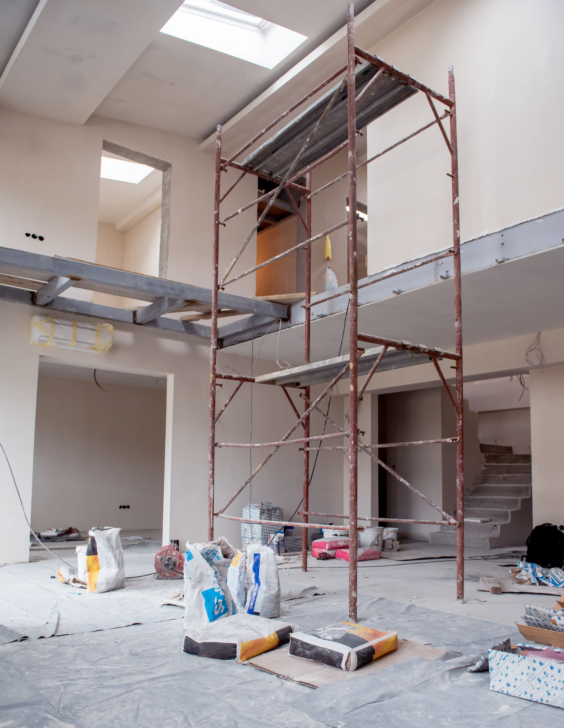 Intérieur d'un bâtiment en construction avec échafaudages. On aperçoit des sacs de matériaux et un escalier.