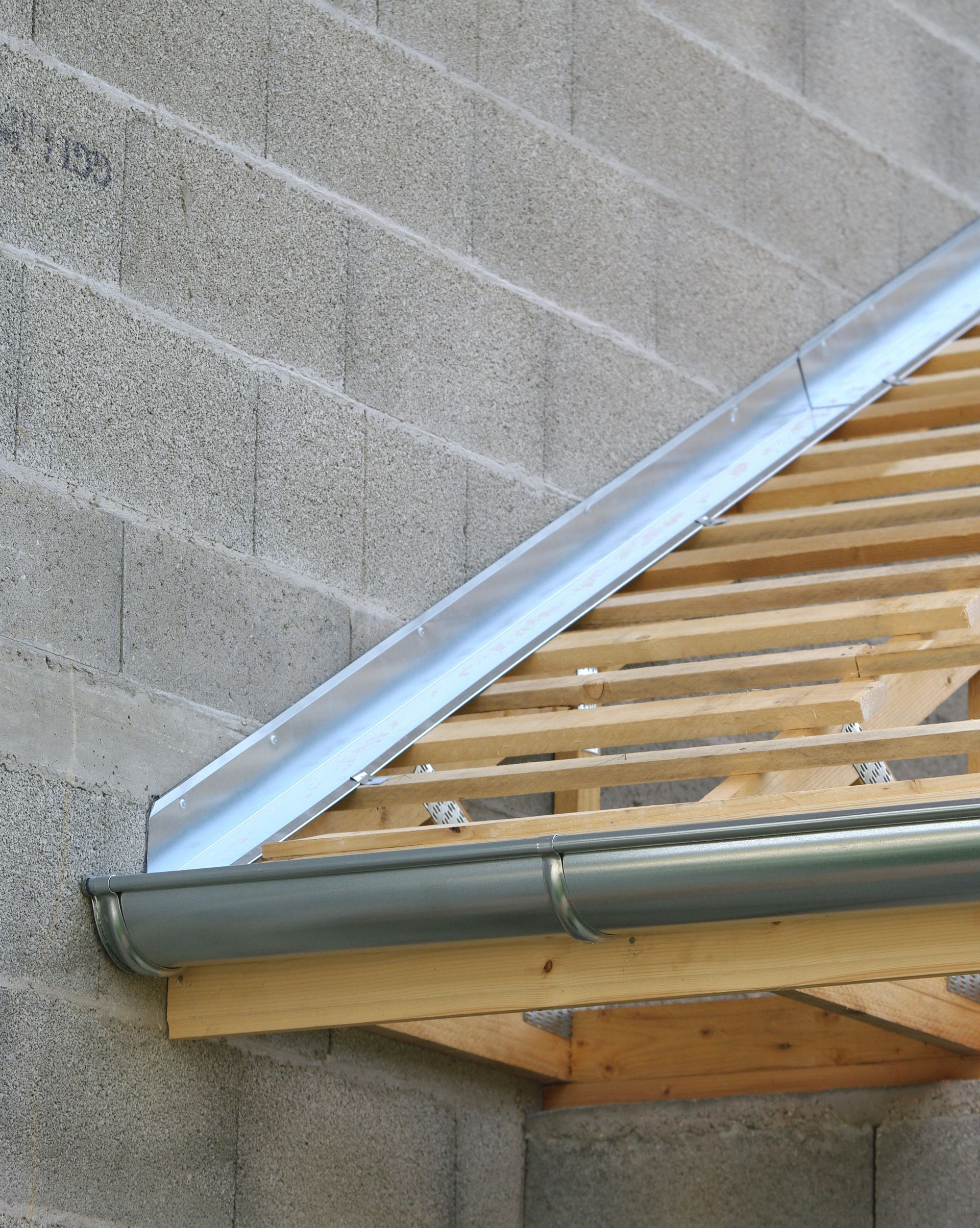 Une bande de solin argentée installée au-dessus d'une gouttière grise fixée à la charpente du toit d'un bâtiment.