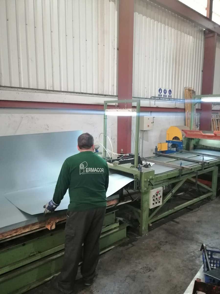 Hombre con camisa verde trabajando con láminas de metal en una fábrica.