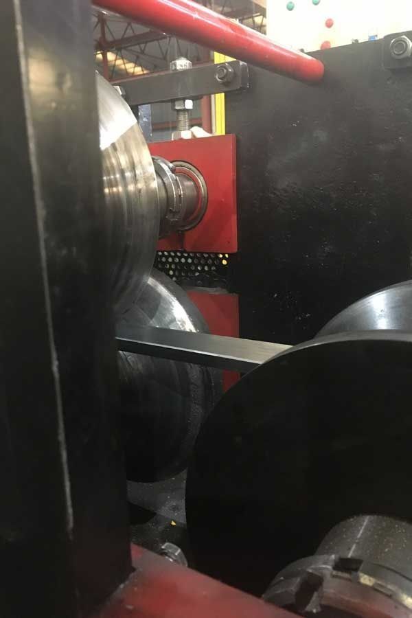 Lámina metálica laminada en rodillos industriales. Maquinaria negra, roja y plateada en una fábrica.