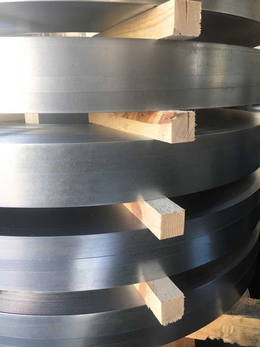 Bobinas de tiras de metal brillante apiladas con soportes de madera.