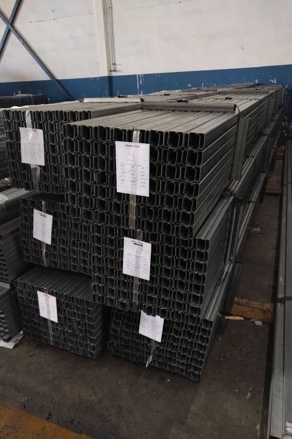 Montones de vigas metálicas en forma de C, agrupadas y etiquetadas, apiladas en un entorno de fábrica.