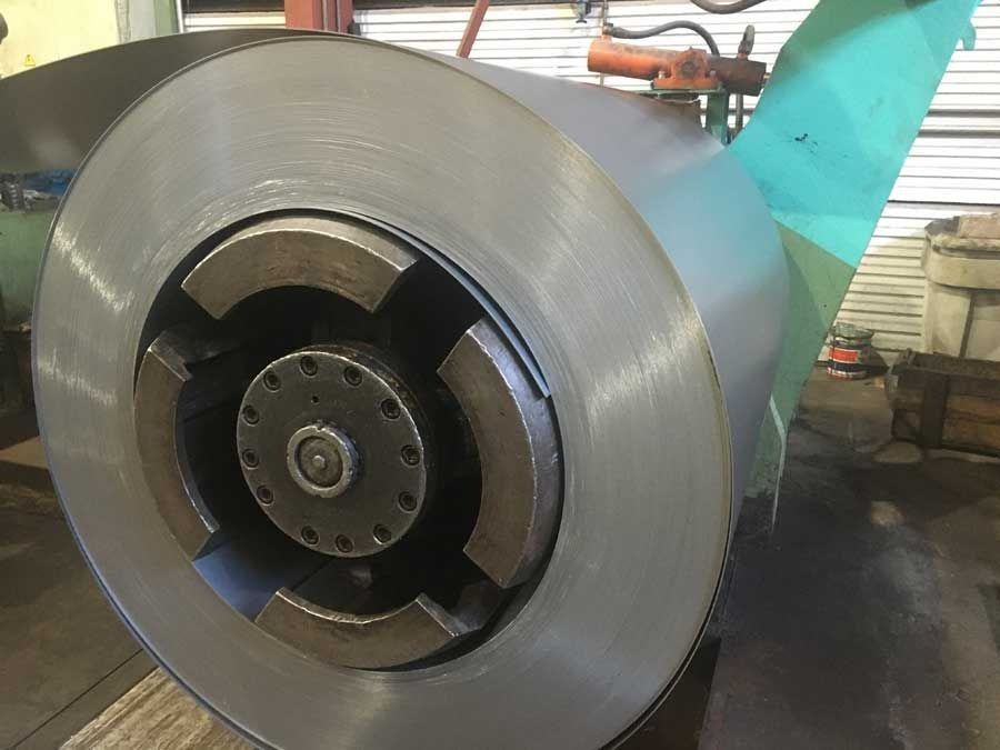 Bobina metálica grande en una máquina. Acero gris y núcleo de metal oscuro. Entorno industrial.