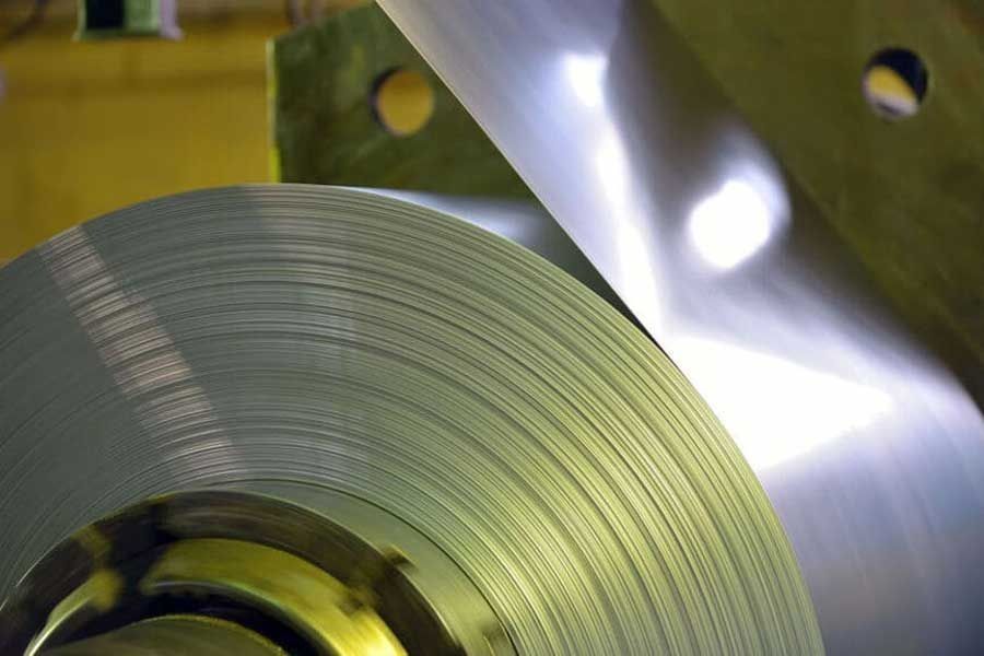 Bobina de metal plateado brillante desenrollándose. Entorno industrial.
