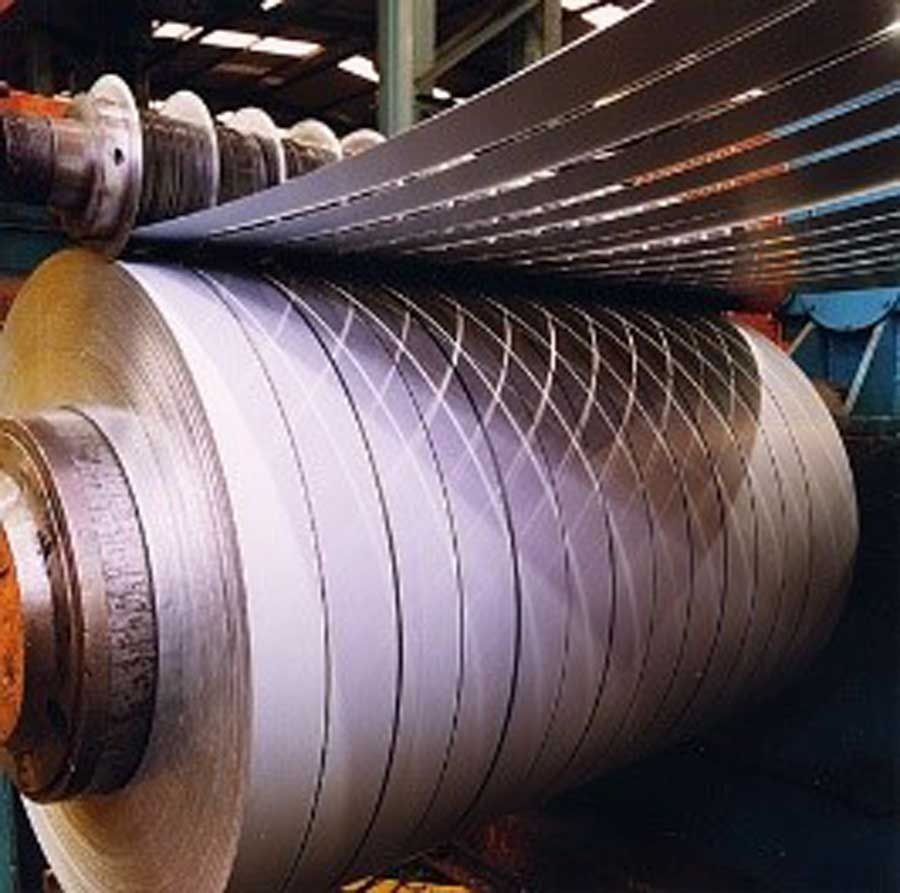 Bobina de metal siendo cortada en tiras por una máquina en una fábrica.