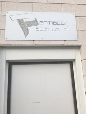 Letrero de Ermacor Aceros SL sobre una puerta blanca; el logotipo presenta una letra