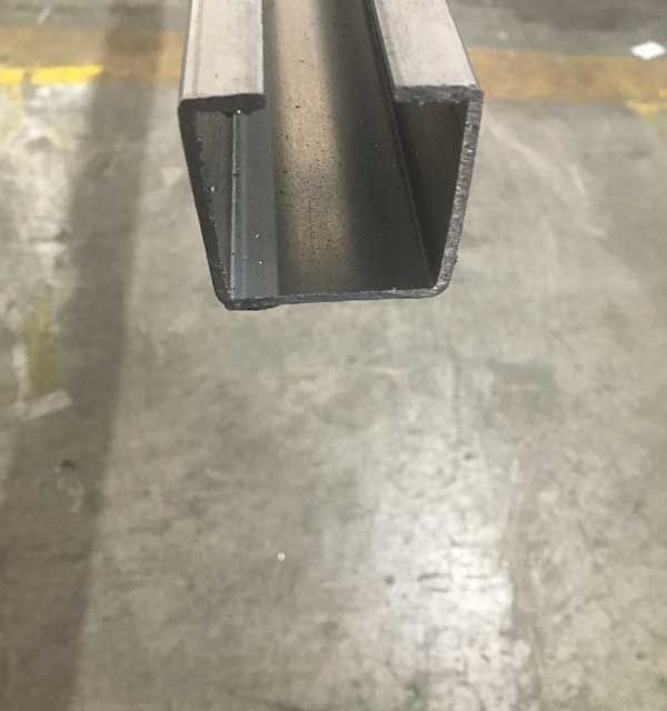 Primer plano de una viga de canal de acero galvanizado. El canal tiene forma de U y reposa sobre un suelo de hormigón.