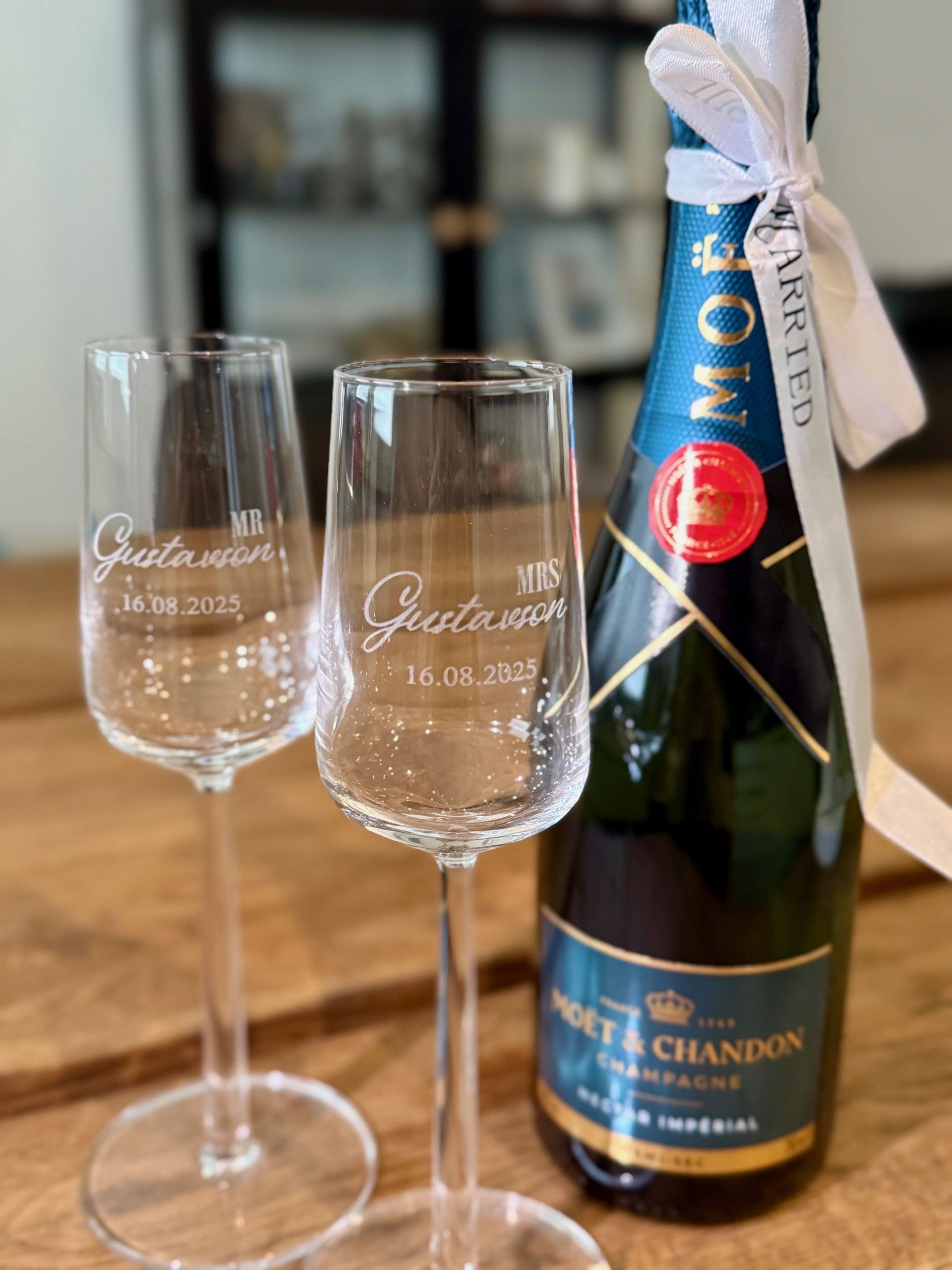 Kaksi kaiverrettua viinilasia Moët & Chandon -samppanjapullon vieressä pöydällä