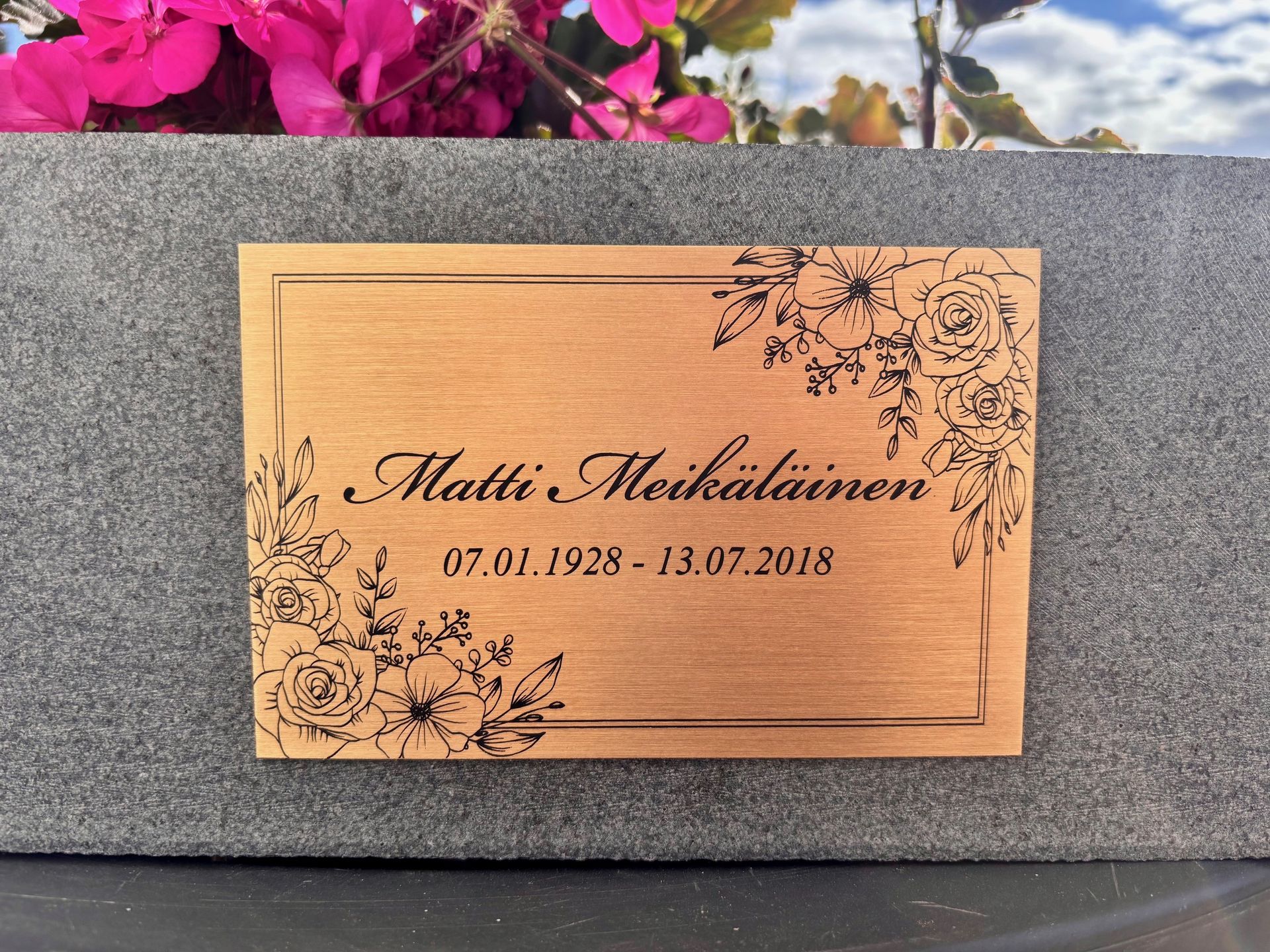 Kuparinen muistolaatta, jossa on kukkakoristeinen kaiverrus ja nimi Matti Mikkola, vuosilta 1971–2018.