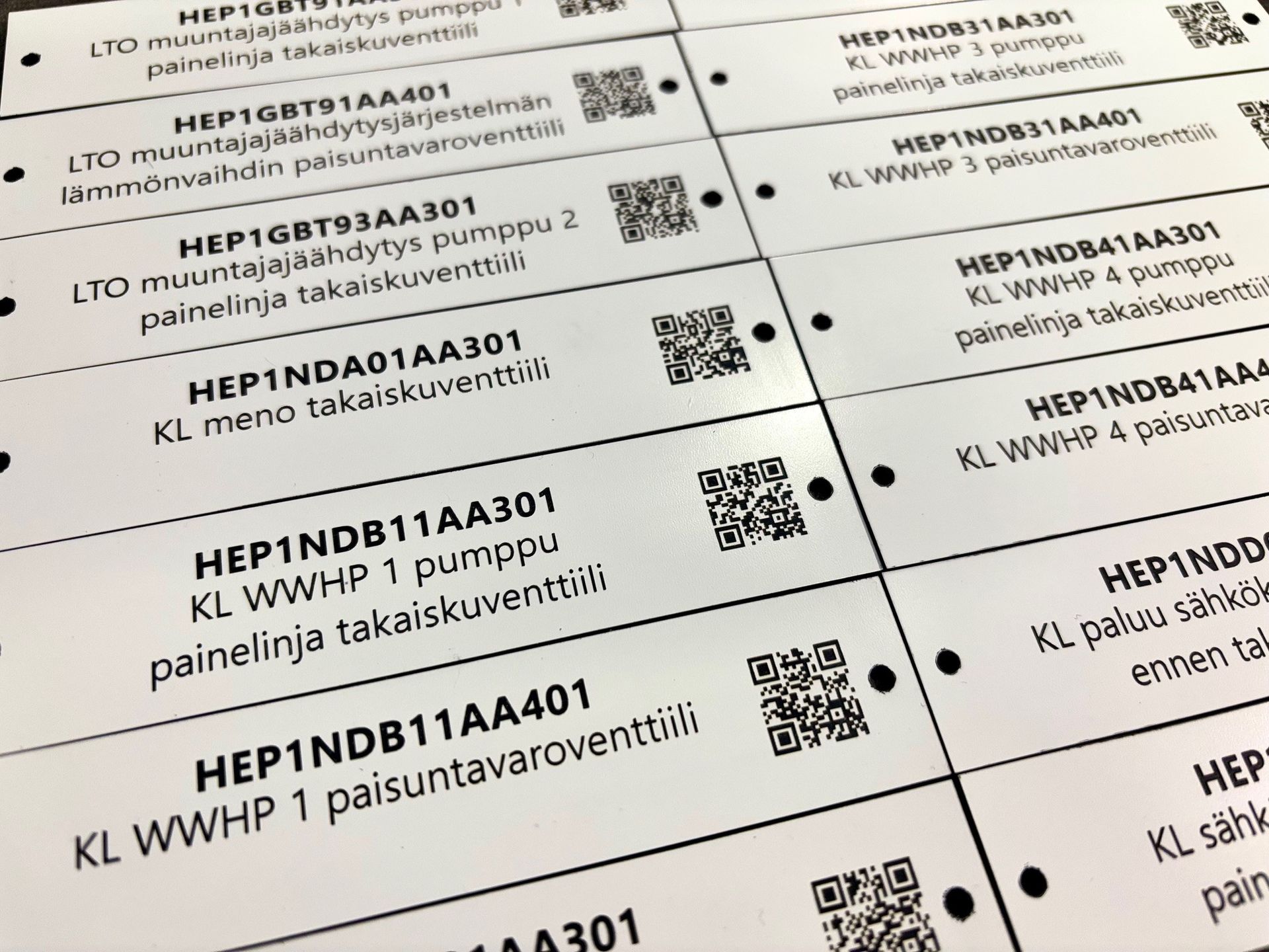 Lähikuva ruutupaperille painetuista etiketeistä, joissa on QR-koodeja ja mustaa tekstiä.